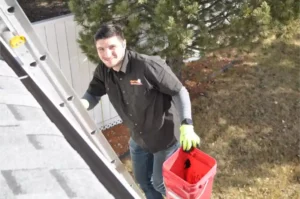 Gutter Cleaning: What to Expect with Darren 1 A Darren Does That employee climbing a ladder with gutter cleaning bucket in hand.