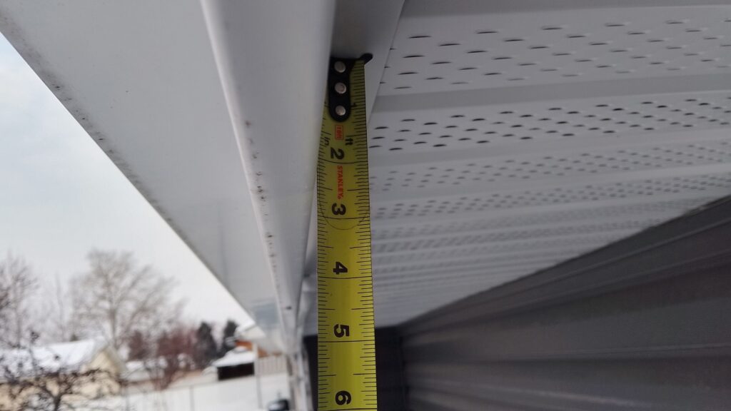 A closeup of the fascia board of an Edmonton home hanging 2.5" below the soffit as seen on a measuring tape, showing that the usual style of Permanent Holiday Light track would be hidden from view.