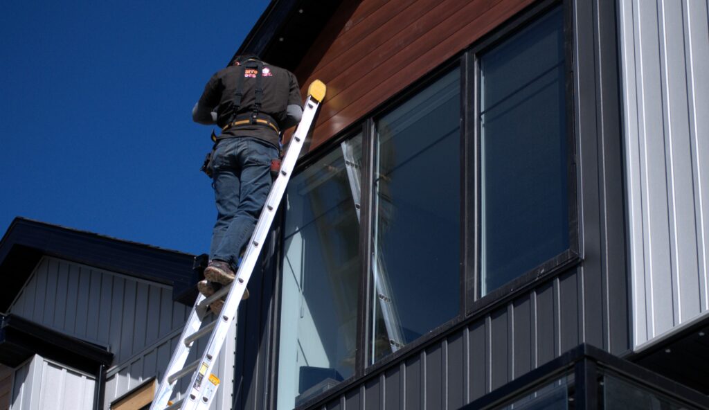 A Darren Does That employee high up on a ladder leaning against the gable of a three story home installing permanent christmas lights in an aluminum track.