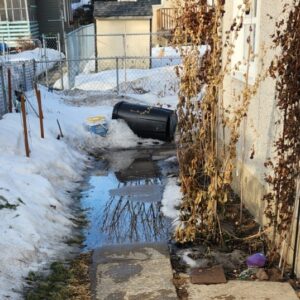 Spring inspection photo showing water pooling on a sidewalk and near a wall during the Spring Thaw, increase the chance of dangerous ice and water infiltration.