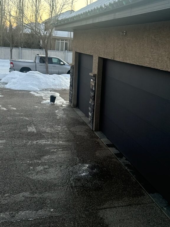 Spring Inspection photo showing mounds of ice on a driveway from leaks in the rain gutters. one in front of a double-wide garage door, and one, much larger under a leaky corner.