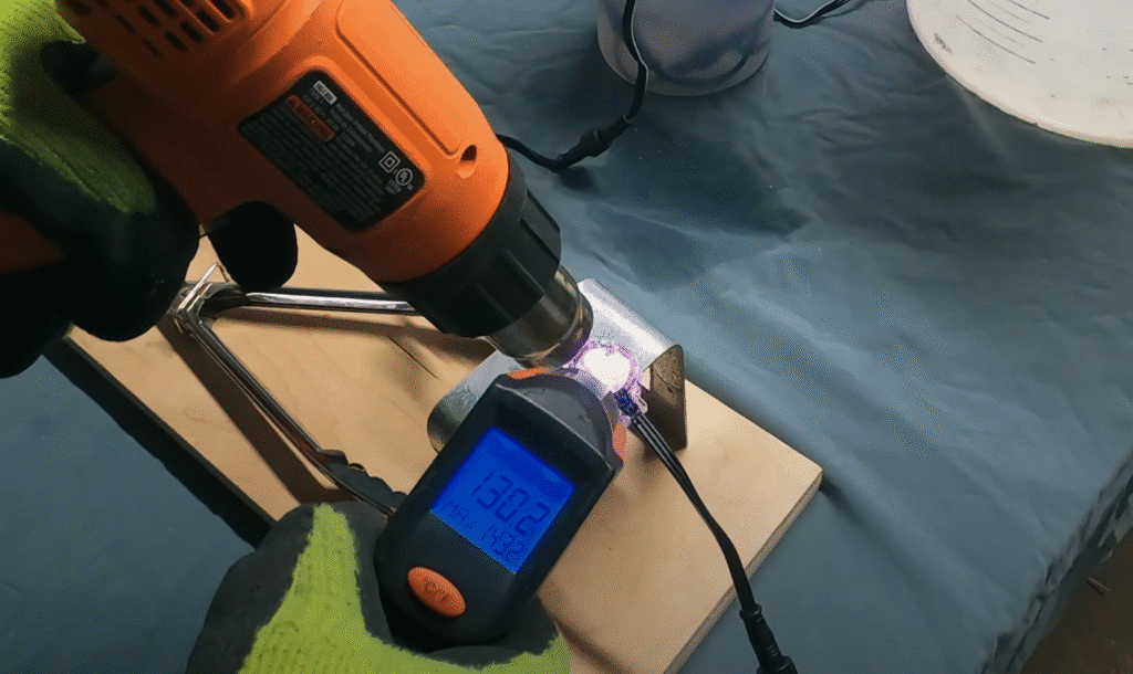 A heat gun is used to apply heat to a Watts Permanent Christmas Light and a thermometer shows the temperature of the light rising over 130 degrees celsius.