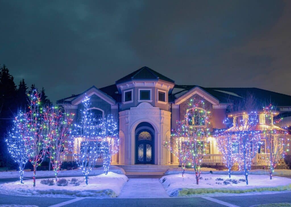 many trees with Christmas Lights in front of an italian style house